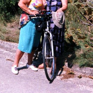 Two women posing with a bicycle outdoors.