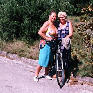 Two women posing with a bicycle outdoors.
