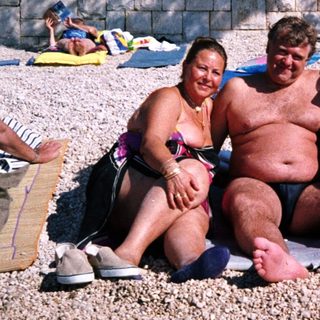 Group of people relaxing shirtless on beach towels.