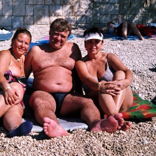 Group of people relaxing shirtless on beach towels.