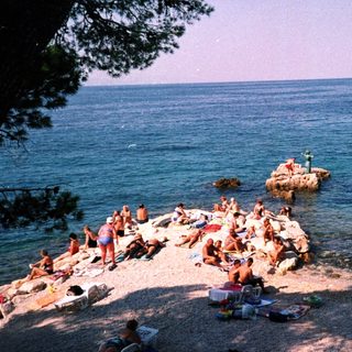 Beach with people sunbathing and swimming in shallow water.