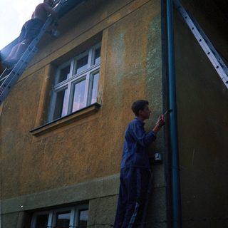 Person cleaning roof gutter from ladder.