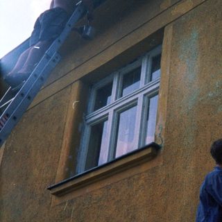 Person cleaning roof gutter from ladder.