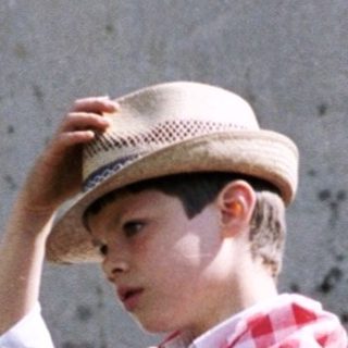 Young boy in festive attire leans on greenery.
