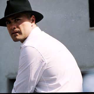 Man in white shirt and fedora near real estate sign.