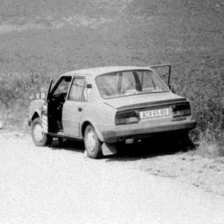 Old car parked on rural road near flooded field.