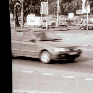 Urban street scene with moving car, parked vehicles, and traffic signs.