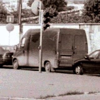 Urban street scene with moving car, parked vehicles, and traffic signs.