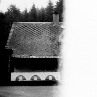 Blurred black-and-white photo of a rustic house with tiled roof.