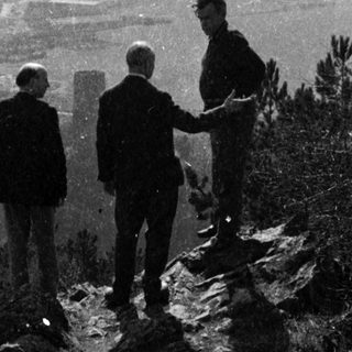 Three men standing on rocky hilltop overlooking landscape.
