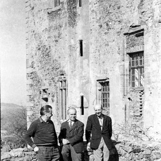 Three men posing outside historic stone building.