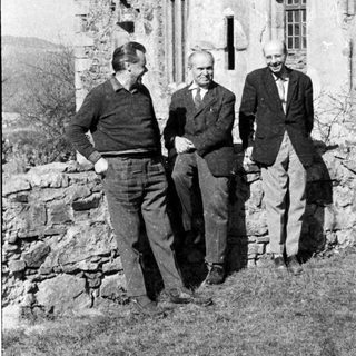Three men posing outside historic stone building.