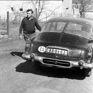 Vintage car with Czech license plate, man standing beside it near rural house.