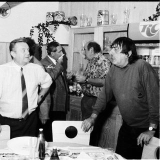 Group of men gathered indoors, socializing and drinking.