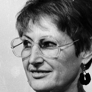 Woman wearing glasses, patterned blouse, and earrings.