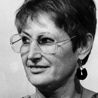 Woman wearing glasses, patterned blouse, and earrings.