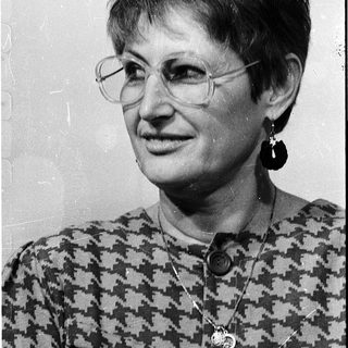 Woman wearing glasses, patterned blouse, and earrings.