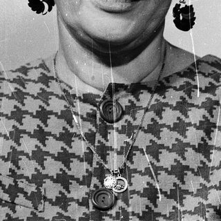 Woman wearing glasses, patterned blouse, dangly earrings.