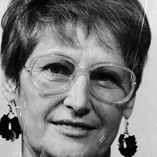 Woman wearing glasses, patterned blouse, and large earrings.
