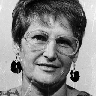 Woman wearing glasses, patterned blouse, and large earrings.
