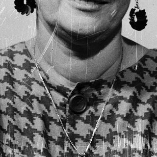 Woman wearing glasses, patterned blouse, and large earrings.