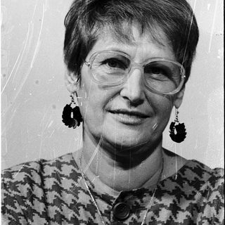 Woman wearing glasses, patterned blouse, and large earrings.