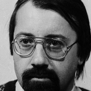 Man in glasses and patterned sweater, serious expression.