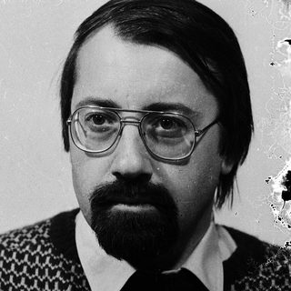 Man in glasses and patterned sweater, serious expression.