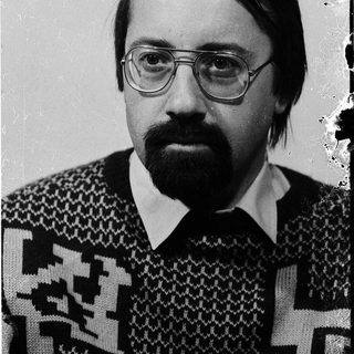 Man in glasses and patterned sweater, serious expression.
