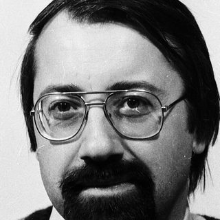 Portrait of a man wearing glasses, sweater, and mustache.