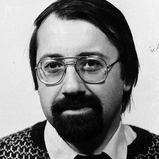 Portrait of a man wearing glasses, sweater, and mustache.