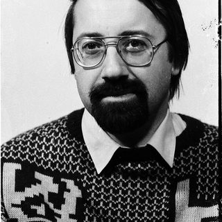 Portrait of a man wearing glasses, sweater, and mustache.