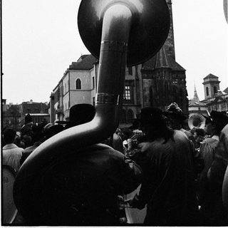 Large brass instrument played in outdoor crowd near historic church tower.