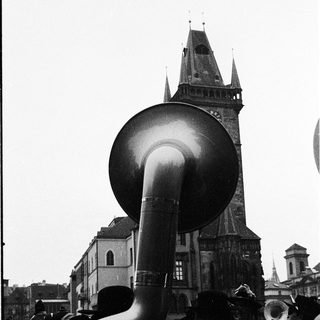 Large brass instrument played in outdoor crowd near historic church tower.