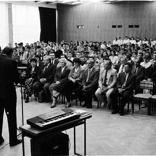 Large audience listens to a speaker at a formal event.