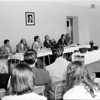 Formal meeting or conference with seated and standing attendees.