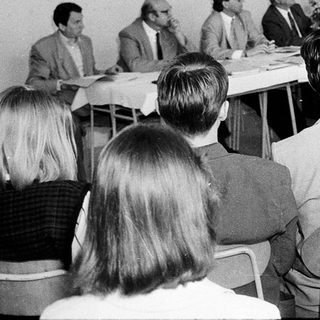 Formal meeting or conference with seated and standing attendees.