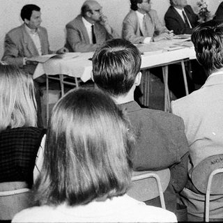 Formal meeting or conference with seated and standing attendees.