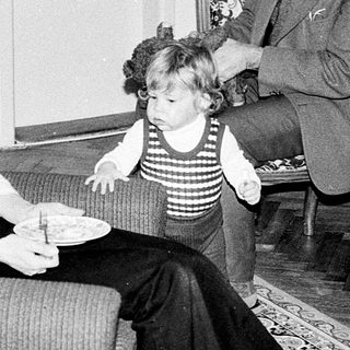 Family moment with man adjusting child's clothing indoors.
