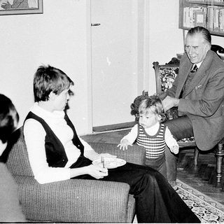 Family moment with man adjusting child's clothing indoors.