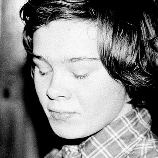 Young woman in plaid shirt, looking thoughtful indoors.
