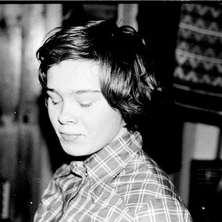 Young woman in plaid shirt, looking thoughtful indoors.
