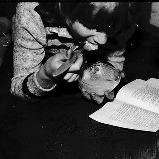 Child carefully reading book with magnifying glass.