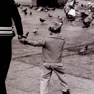 Boy feeding pigeons in city square.