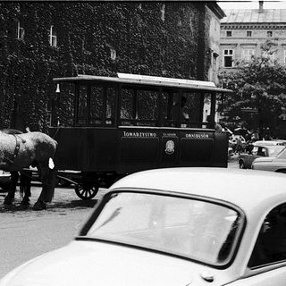 Horse-drawn tram in urban street scene.