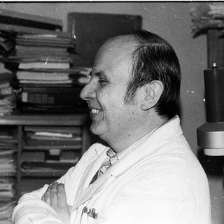 Man in lab coat smiling in office setting.