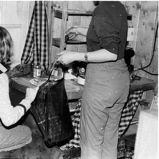 Two women preparing food indoors using vintage kitchen tools.