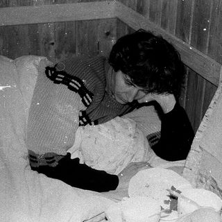 Person sleeping on makeshift bed in damaged, ruined room.