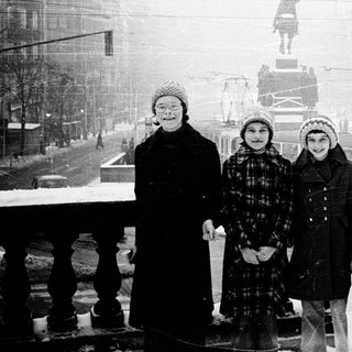 Three children pose in winter snow near historic city statue.