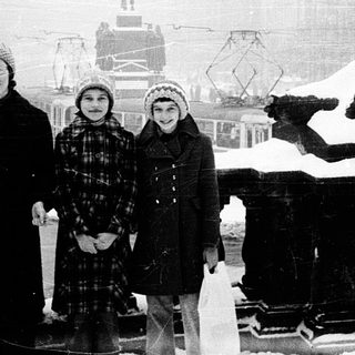 Three children pose in winter snow near historic city statue.